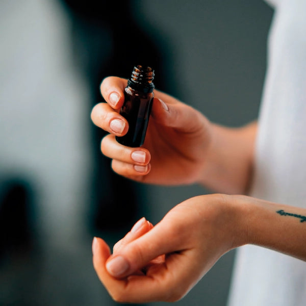 Person holding a small amber bottle with a dropper, essential oils