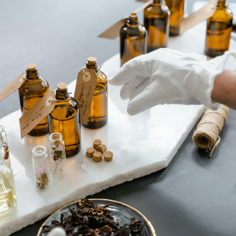 Bottles of oils on a marble slab with a hand in a white glove, on a gray surface.